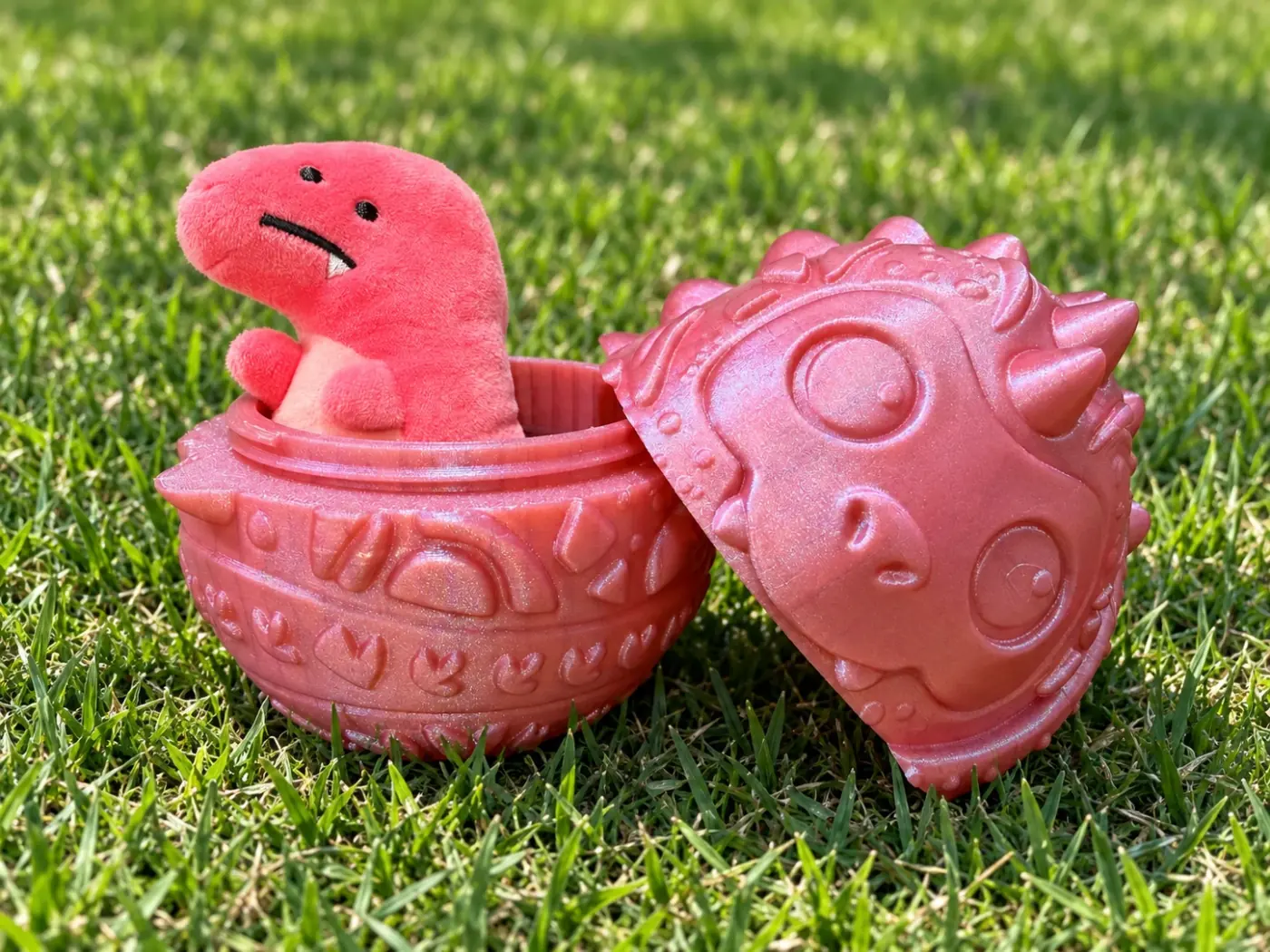 A printed red dragon egg, opened, with a plush dinosaur peeking out of the bottom half